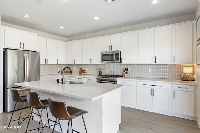 kitchen with appliances with stainless steel finishes, a sink, white cabinets, light wood-style flooring, and backsplash