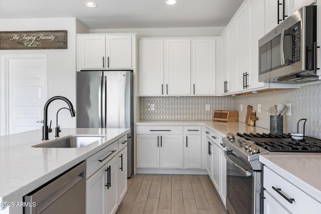 kitchen with stainless steel appliances, a sink, white cabinetry, decorative backsplash, and recessed lighting