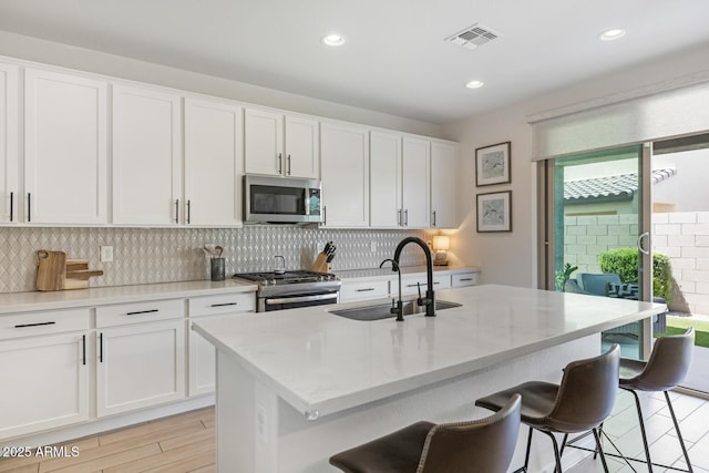 kitchen with a sink, stainless steel appliances, decorative backsplash, a kitchen bar, and recessed lighting