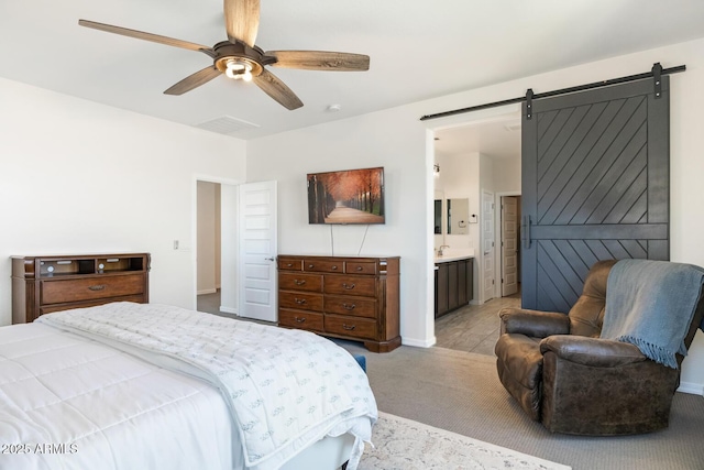 bedroom with light colored carpet, ceiling fan, connected bathroom, a barn door, and baseboards