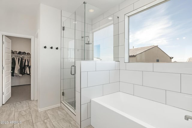bathroom with a walk in closet, a shower stall, a bath, marble finish flooring, and baseboards