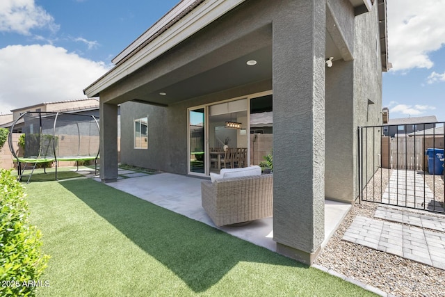 back of house featuring a trampoline, stucco siding, a patio area, and a gate