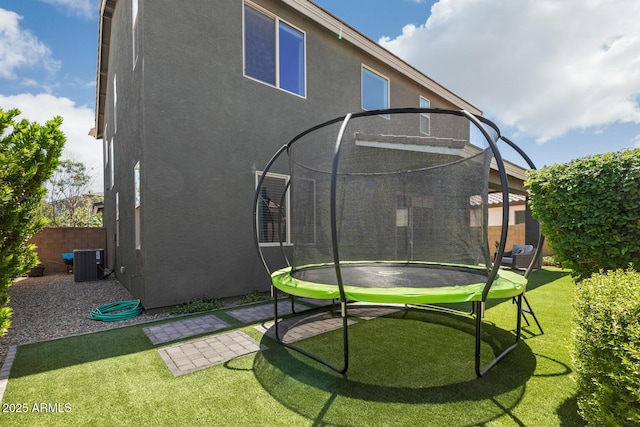 back of house featuring a trampoline, stucco siding, and central air condition unit
