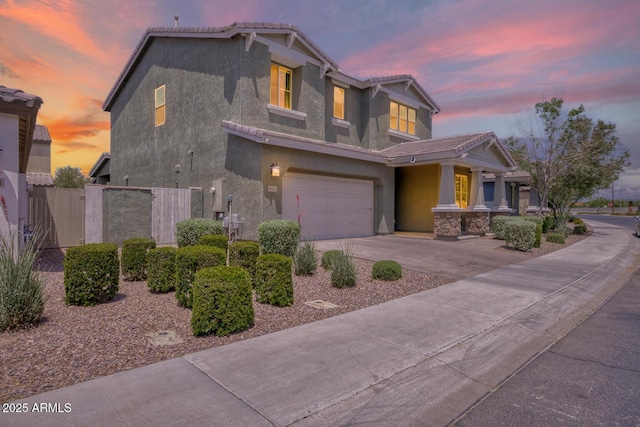 view of front of home featuring stucco siding, a tiled roof, concrete driveway, a garage, and fence