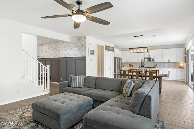 living area featuring wood finished floors, a ceiling fan, stairway, and wainscoting