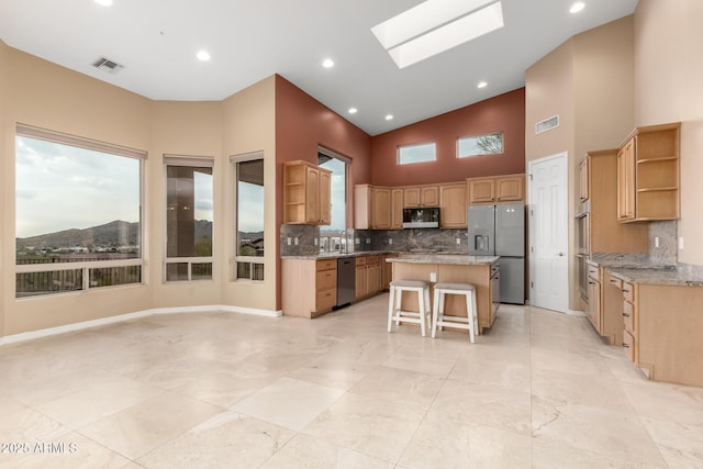 kitchen featuring appliances with stainless steel finishes, a skylight, a breakfast bar area, decorative backsplash, and a center island