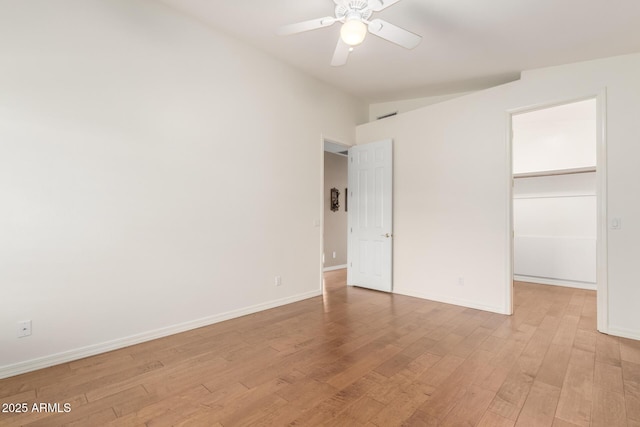 unfurnished bedroom featuring ceiling fan, a walk in closet, a closet, and light hardwood / wood-style flooring