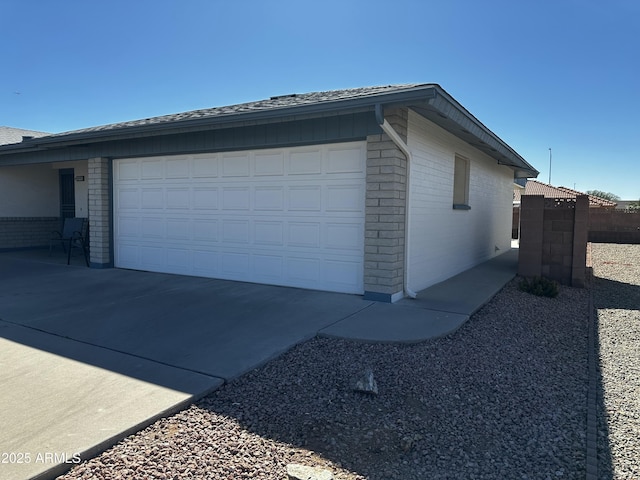 view of home's exterior featuring concrete driveway, brick siding, roof with shingles, and fence