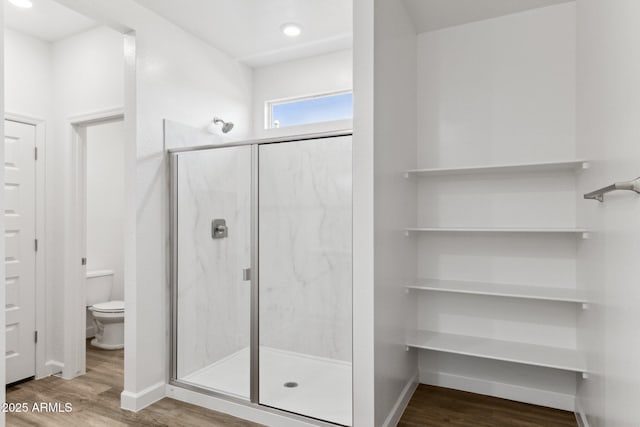 bathroom featuring hardwood / wood-style flooring, a shower with shower door, and toilet