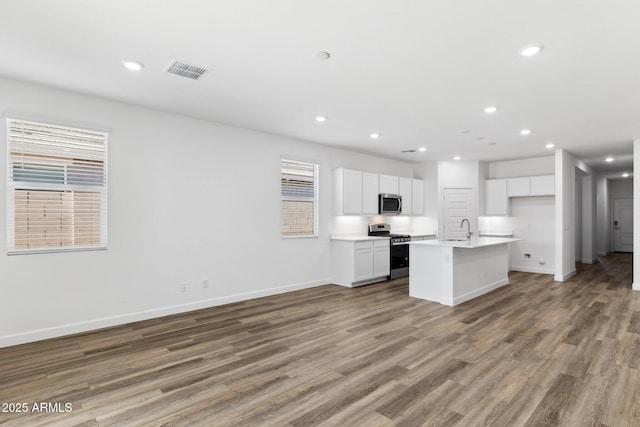 kitchen with sink, white cabinetry, hardwood / wood-style floors, stainless steel appliances, and a kitchen island with sink