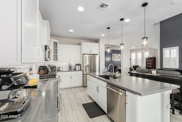 kitchen featuring sink, decorative light fixtures, a center island with sink, stainless steel appliances, and white cabinets