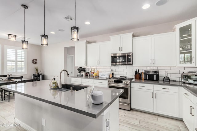 kitchen with sink, hanging light fixtures, stainless steel appliances, a kitchen island with sink, and white cabinets