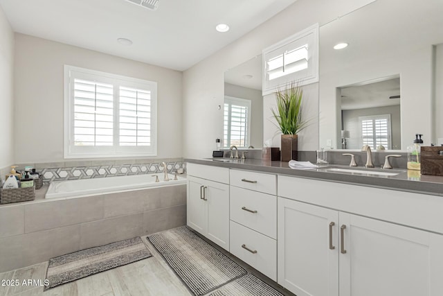 bathroom with hardwood / wood-style flooring, a healthy amount of sunlight, vanity, and tiled tub