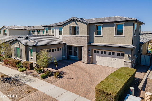 view of front of home featuring stone siding, decorative driveway, a tiled roof, and stucco siding