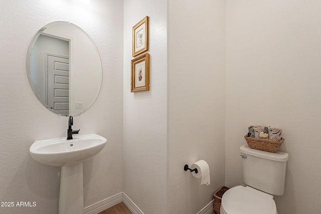 half bathroom featuring wood finished floors, toilet, and baseboards