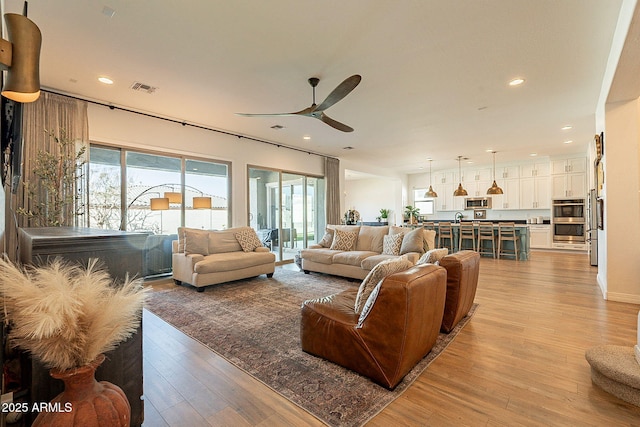 living area with light wood-style flooring, a ceiling fan, visible vents, and recessed lighting