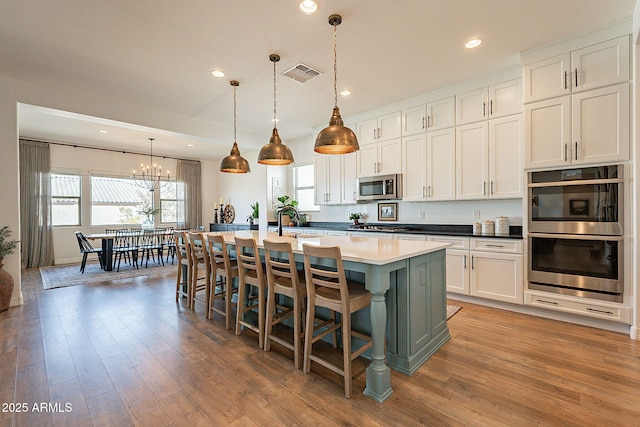 kitchen featuring stainless steel appliances, light wood-type flooring, visible vents, and an island with sink