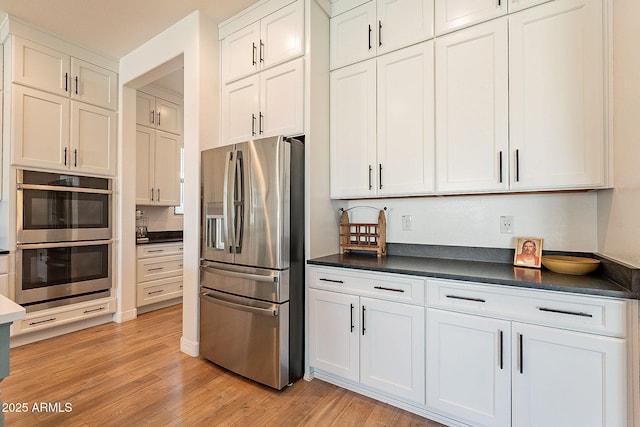 kitchen with stainless steel appliances, dark countertops, light wood-type flooring, and white cabinetry