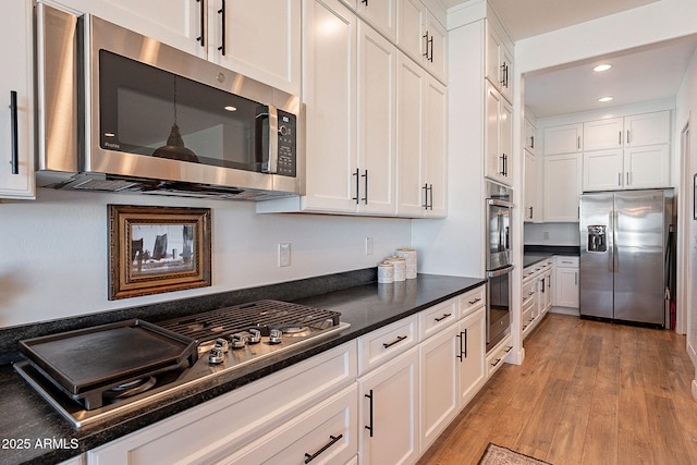 kitchen with dark countertops, appliances with stainless steel finishes, light wood-type flooring, and white cabinets