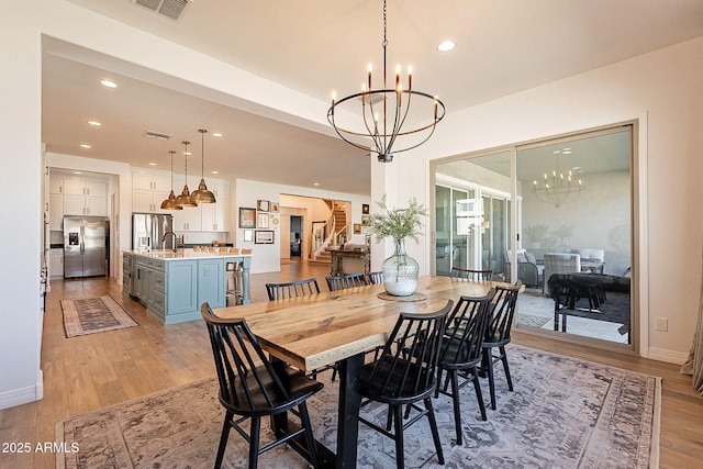 dining space featuring light wood-style flooring, stairs, visible vents, and a notable chandelier