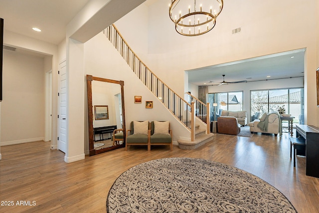 foyer entrance with visible vents, stairway, wood finished floors, baseboards, and ceiling fan with notable chandelier