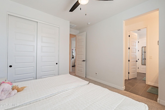 bedroom featuring carpet floors, a ceiling fan, baseboards, a closet, and tile patterned floors