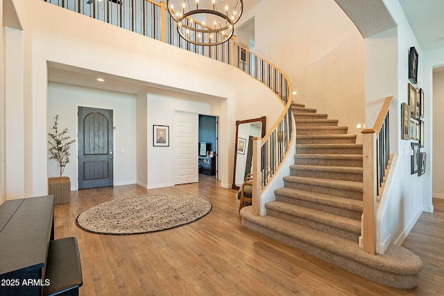 foyer with a notable chandelier, wood finished floors, a towering ceiling, baseboards, and stairs