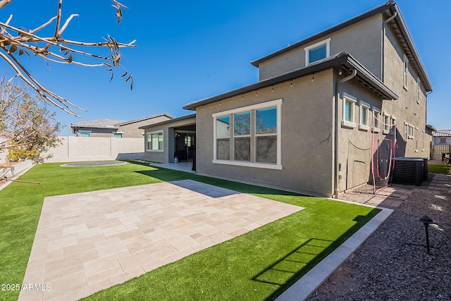 rear view of house with central AC unit, fence, a yard, stucco siding, and a patio area