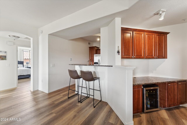 kitchen featuring stainless steel fridge, a breakfast bar, dark stone countertops, dark hardwood / wood-style floors, and wine cooler