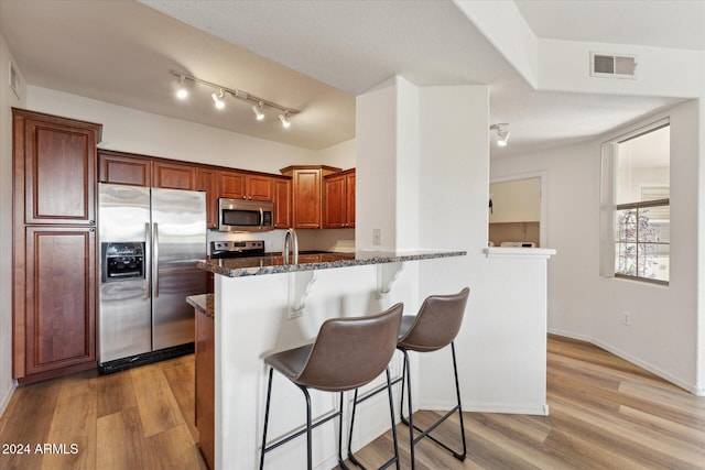 kitchen featuring dark stone counters, kitchen peninsula, stainless steel appliances, and light wood-type flooring