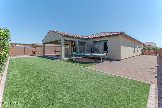 rear view of property with a lawn, a patio, and a trampoline