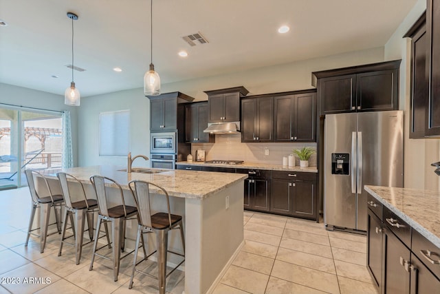 kitchen with decorative light fixtures, a kitchen island with sink, a breakfast bar area, appliances with stainless steel finishes, and light tile patterned flooring