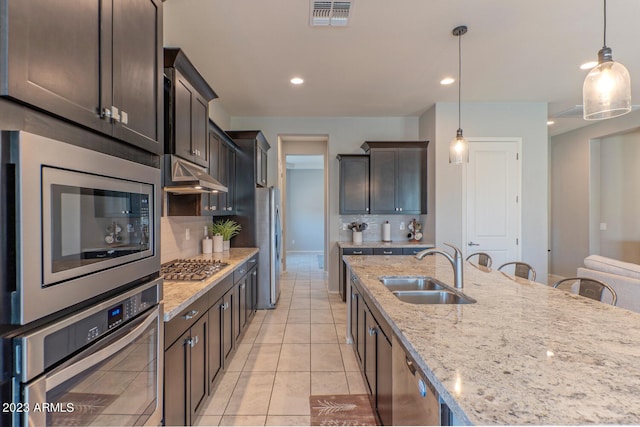 kitchen featuring appliances with stainless steel finishes, light stone countertops, light tile patterned floors, sink, and dark brown cabinets