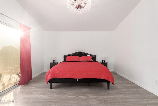 bedroom with vaulted ceiling, an inviting chandelier, and light hardwood / wood-style flooring