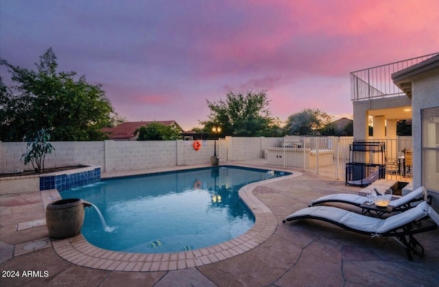 pool at dusk with a patio area and pool water feature