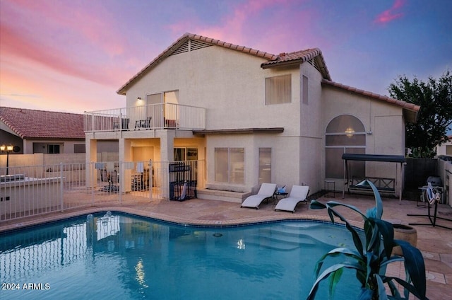 back house at dusk featuring a fenced in pool, a patio, and a balcony