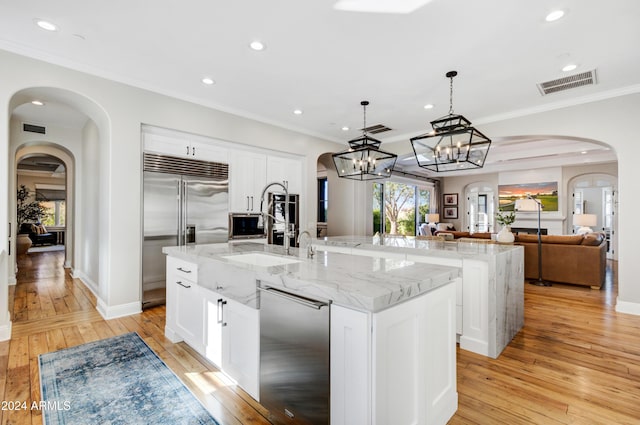 kitchen with appliances with stainless steel finishes, a large island with sink, light hardwood / wood-style floors, white cabinetry, and hanging light fixtures