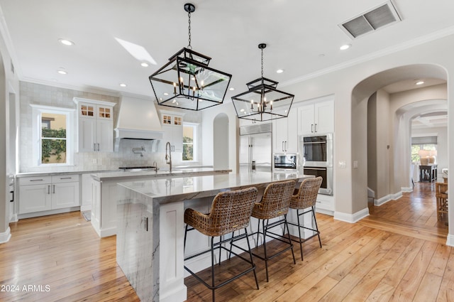 kitchen with white cabinets, custom range hood, built in appliances, and light hardwood / wood-style floors