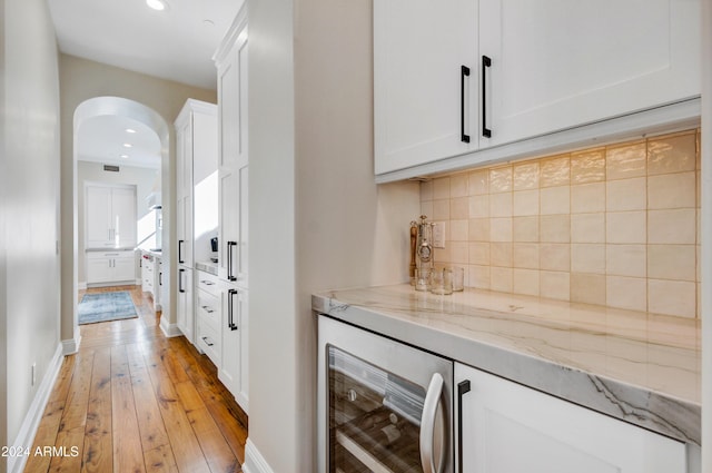 bar with white cabinetry, light stone countertops, beverage cooler, and light hardwood / wood-style floors