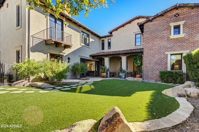 rear view of property featuring a yard and a balcony