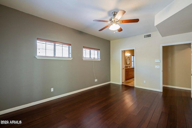 unfurnished bedroom featuring ensuite bath, multiple windows, dark wood-type flooring, and ceiling fan