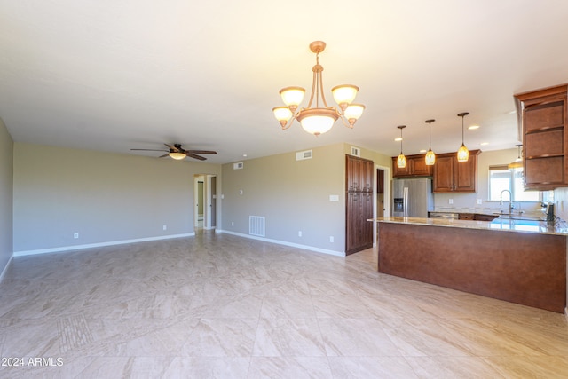 kitchen with sink, stainless steel refrigerator with ice dispenser, ceiling fan with notable chandelier, light stone countertops, and decorative light fixtures