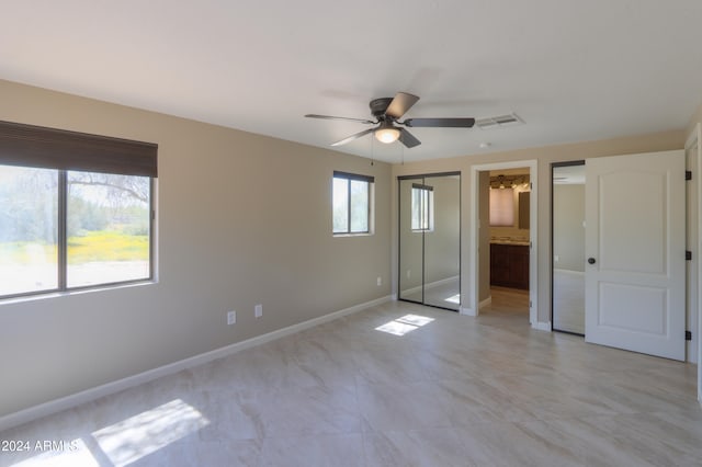 unfurnished bedroom with a closet, multiple windows, ceiling fan, and ensuite bath