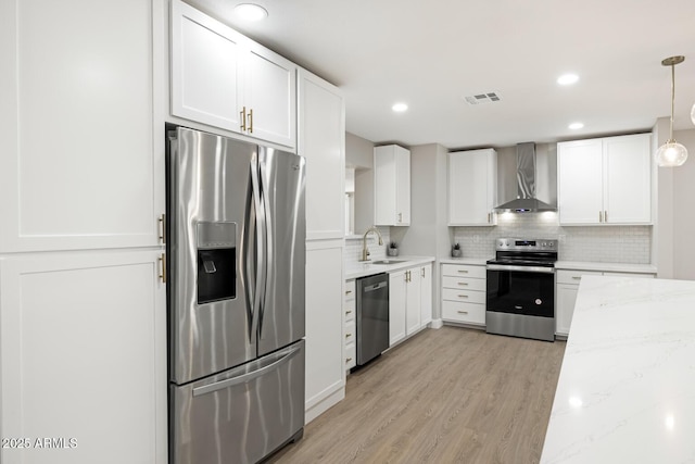 kitchen with light wood finished floors, wall chimney exhaust hood, light stone counters, stainless steel appliances, and white cabinetry