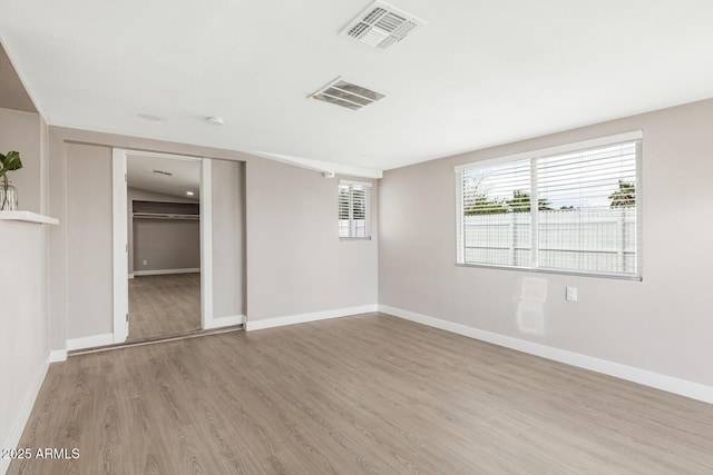 empty room with light wood-style flooring, visible vents, and baseboards