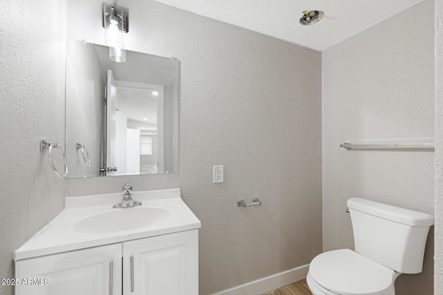 bathroom with a textured wall, toilet, vanity, wood finished floors, and baseboards