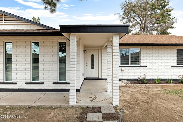 view of exterior entry featuring roof with shingles and brick siding