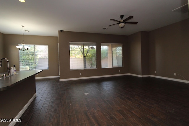 unfurnished living room featuring dark wood-type flooring, ceiling fan with notable chandelier, and sink