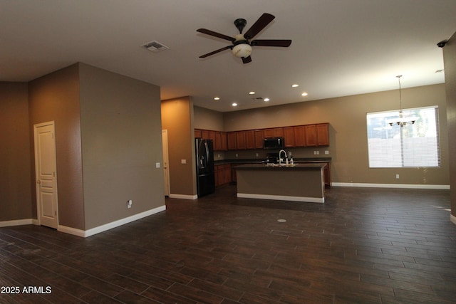 kitchen featuring dark wood-type flooring, sink, black refrigerator with ice dispenser, hanging light fixtures, and a center island with sink