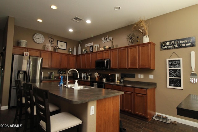 kitchen with appliances with stainless steel finishes, dark hardwood / wood-style floors, sink, a kitchen bar, and a center island with sink